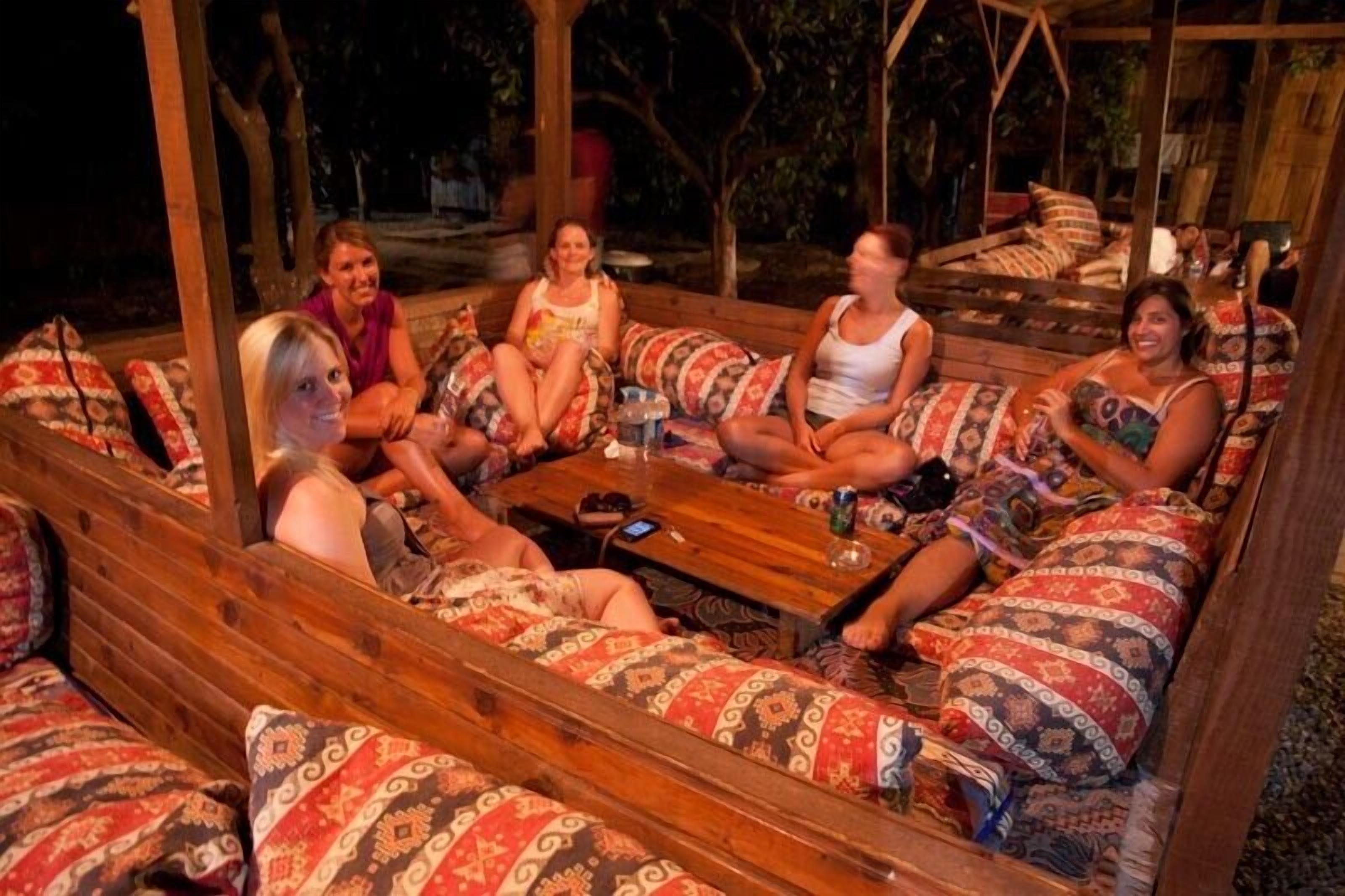 A group of people seated on patterned sofas around a wooden table in an outdoor setting.