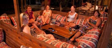 A group of people seated on patterned sofas around a wooden table in an outdoor setting.