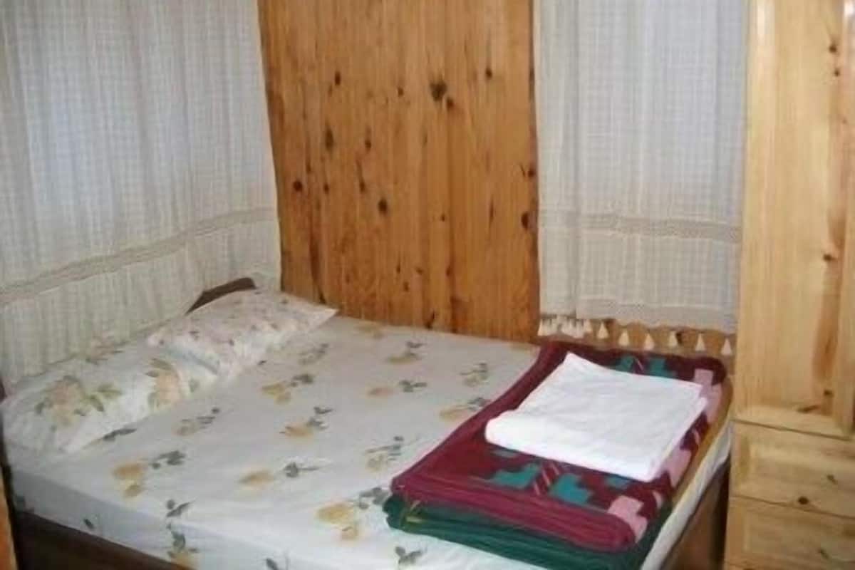 Una cama individual con colcha estampada, cabecera de madera y mesita de noche con lámpara.