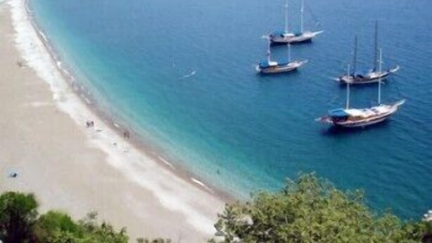 A beach with clear turquoise waters and several sailboats anchored near the shore. - Bayrams Tree Houses (Kumluca)