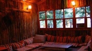 A cozy room with a wooden wall, a cushioned bench, and a patterned rug. - Bayrams Tree Houses (Kumluca)