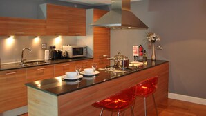 A modern kitchen with wooden cabinets, a stainless steel range hood, a microwave, and a central island with bar stools. - Dreamhouse Apartments Glasgow City Centre (Glasgow)