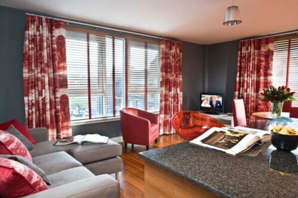 A modern living room with a grey sofa, red chair, and a dining area with a table and chairs.