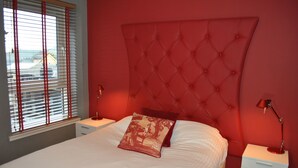 A bedroom with a red headboard, white bedding, and a window with blinds. - Dreamhouse Apartments Glasgow City Centre (Glasgow)