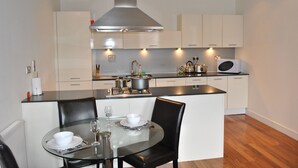 A modern kitchen with a central island, stainless steel appliances, and a dining area with a glass table and black chairs. - Dreamhouse Apartments Glasgow City Centre (Glasgow)