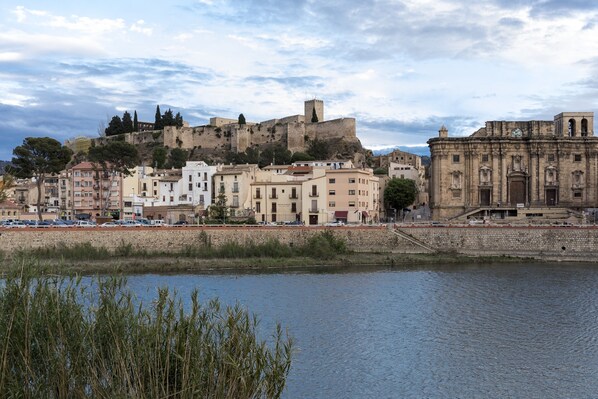 A historic cityscape with a prominent castle on a hill, a river in the foreground, and a mix of traditional and modern buildings. - Parador de Tortosa (Tortosa)