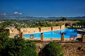 Une piscine bordée d’un mur en pierre, offrant une vue sur des collines lointaines.