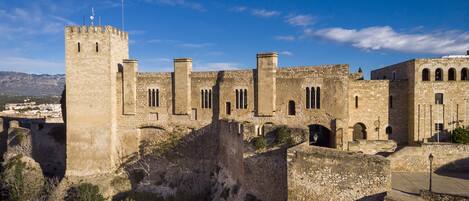 Un castillo de piedra histórico con múltiples torres y ventanas de arco, rodeado de terreno rocoso y vegetación escasa.