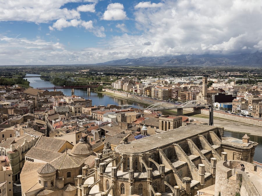 Een historisch stadsgezicht met een opvallende kathedraal, een rivier en bergen op de achtergrond.