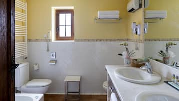 Een badkamer met toilet, wastafel en bad. Boven het toilet is een raam, er is een handdoekhouder en een spiegel met een handdoek.