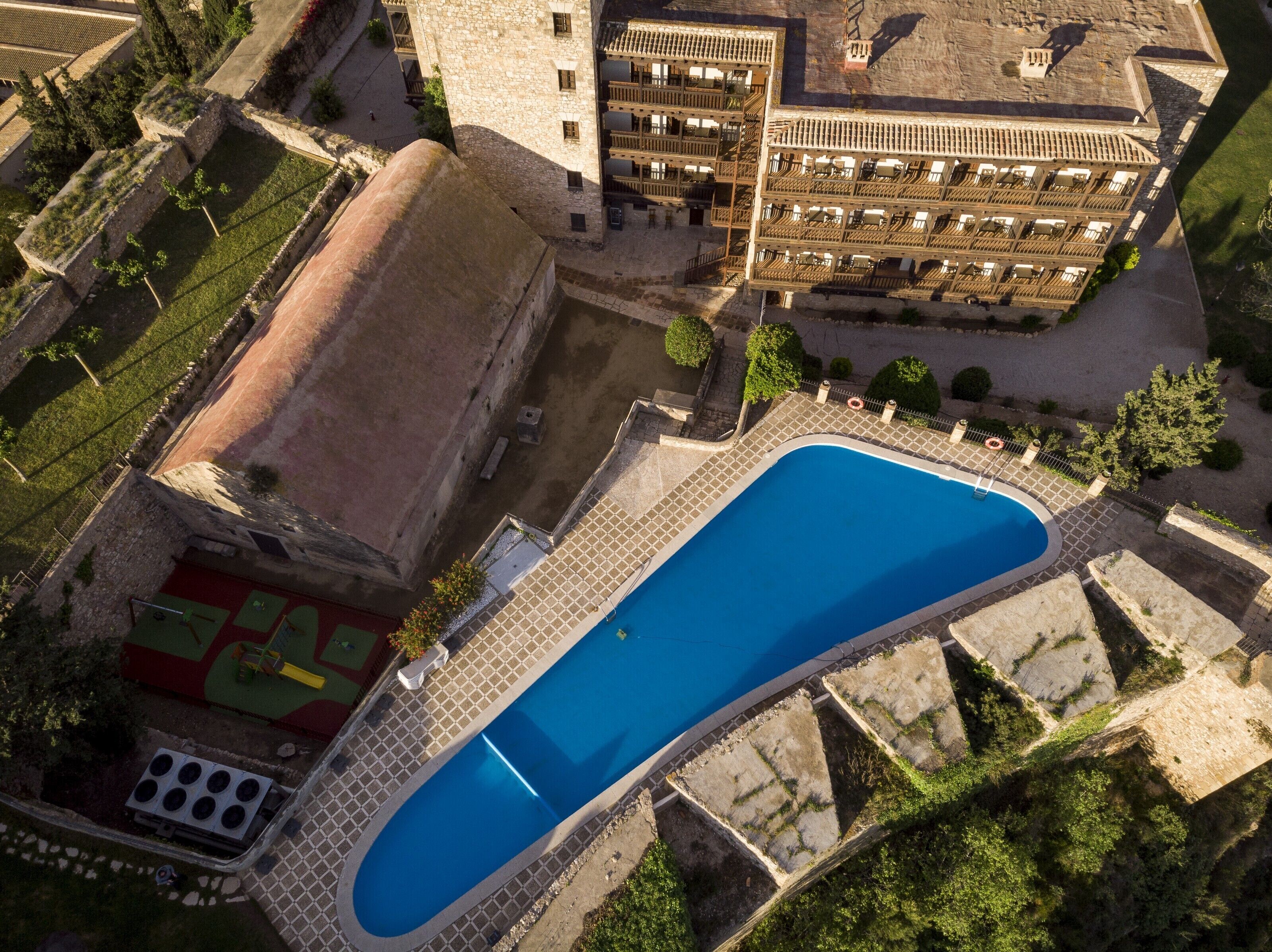 Vista aérea de un hotel con una piscina grande, un patio interior y un edificio con varios balcones.