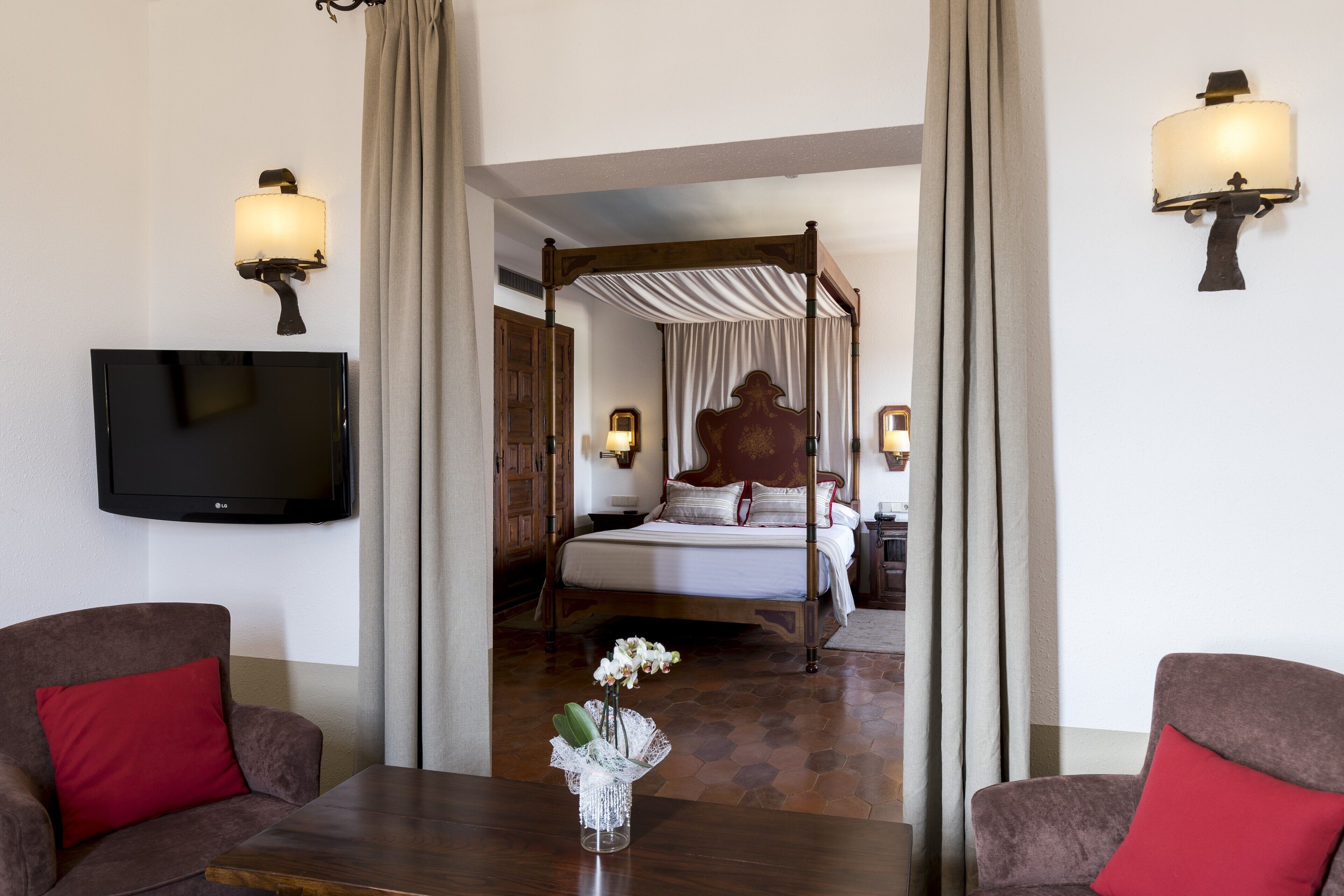Una camera d'albergo con un letto a baldacchino, una TV a schermo piatto e un tavolo da pranzo con un vaso di fiori.