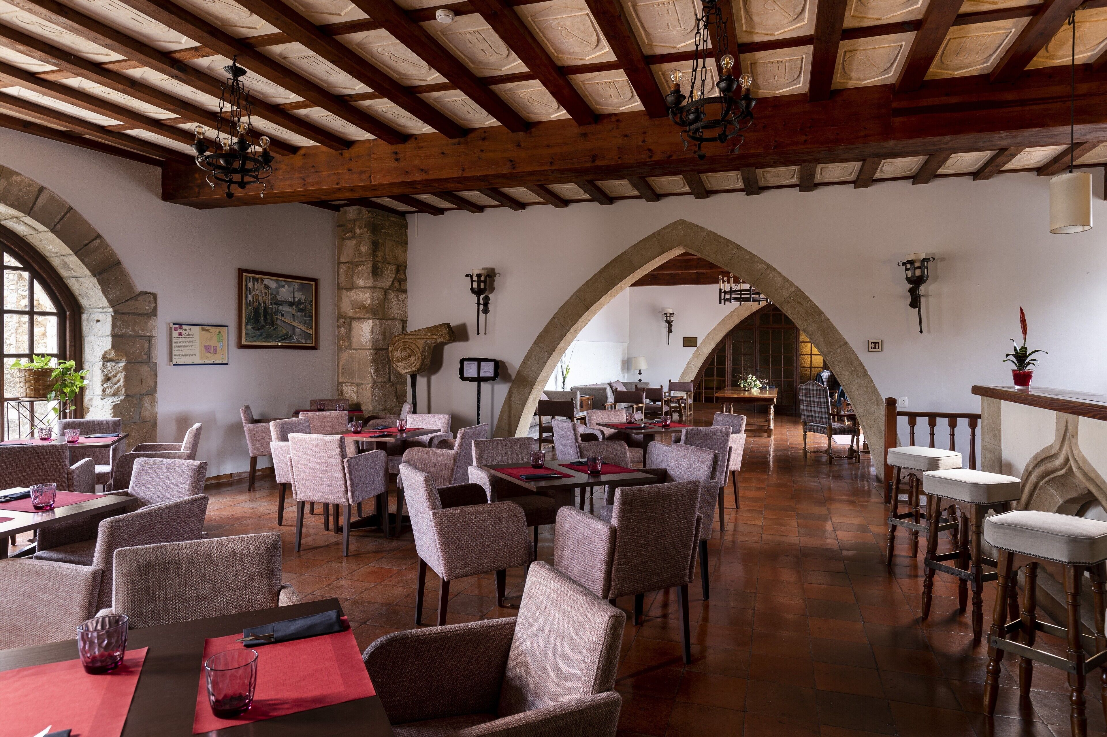 Una àmplia zona de dinar amb alts bigues de fusta, arcs de pedra i lluminàries modernes.