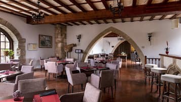 Uma ampla sala de jantar com vigas de madeira altas, arcos de pedra e luminárias modernas.