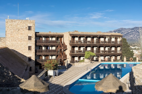 A traditional stone building with multiple balconies, a swimming pool, and a mountainous backdrop. - Parador de Tortosa (Tortosa)