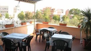 A rooftop terrace with tables and chairs, potted plants, and a view of buildings. - Torre Clementina (Fiumicino)