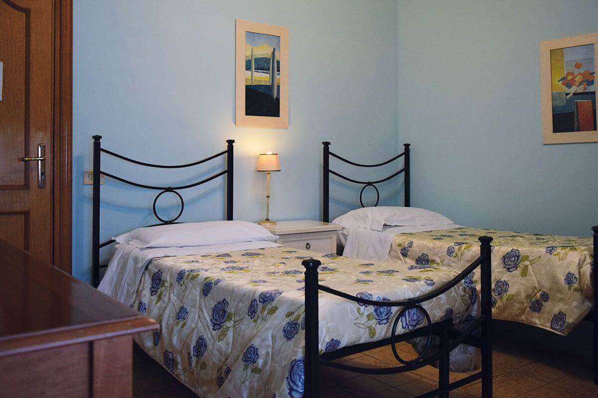 A bedroom with two single beds, a nightstand, a lamp, and two framed pictures on the wall.