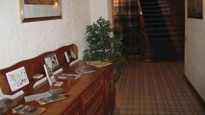 A reception desk with a framed painting above it, a potted plant to the right, and a staircase leading to an upper floor. - Torre Clementina (Fiumicino)