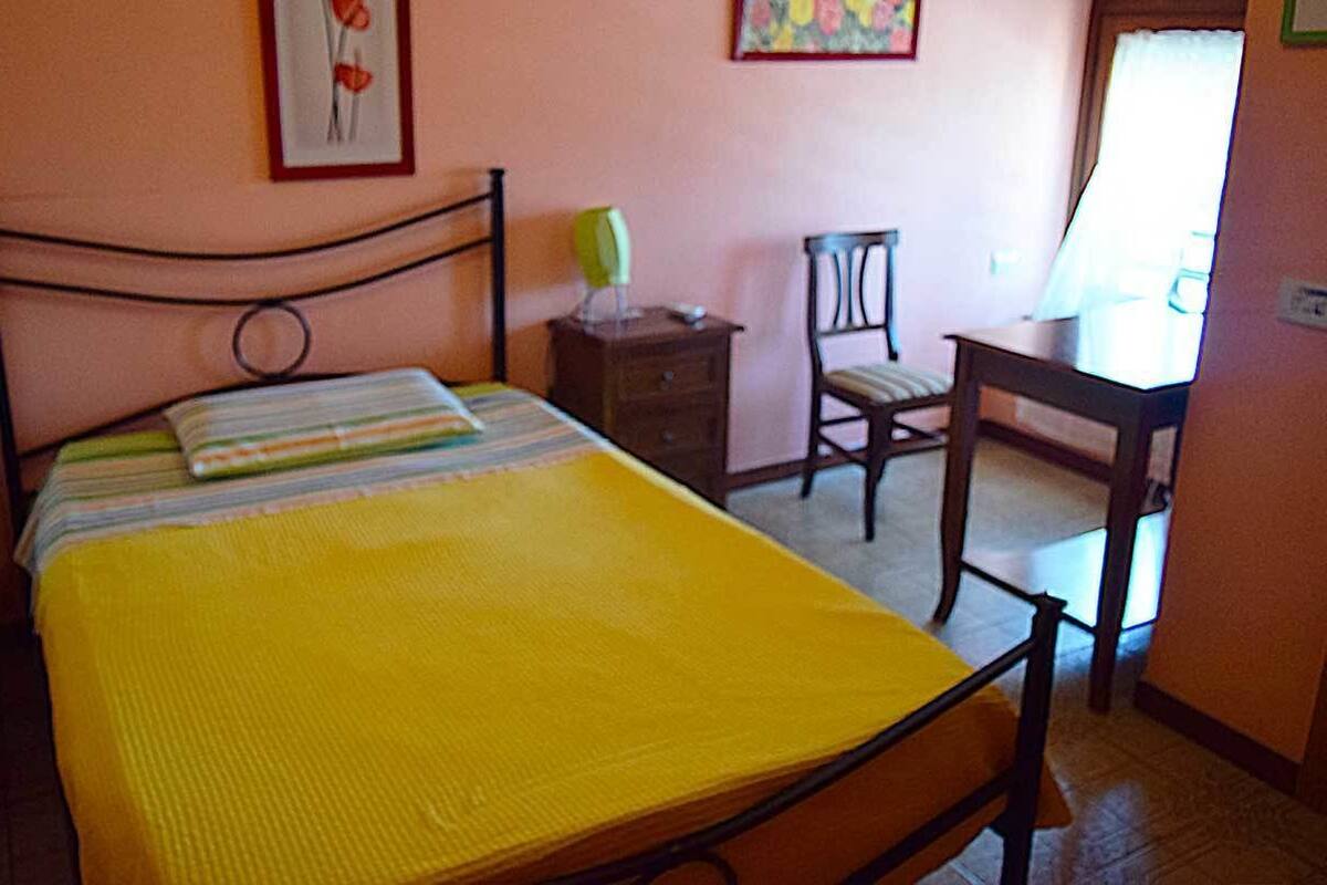 A bedroom with a bed, a chair, a small table, and a radiator.