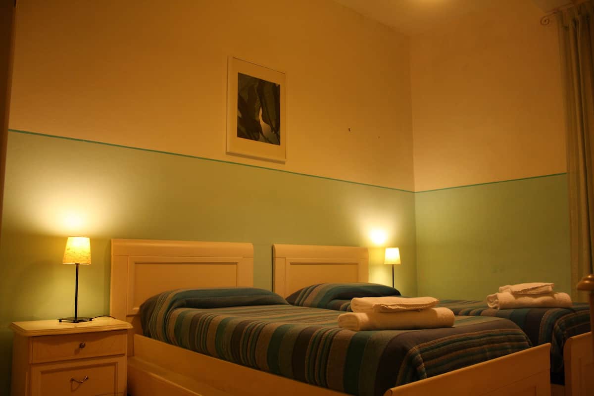 Habitación de hotel con dos camas, cada una con ropa de cama a rayas, una mesita de noche con una lámpara y un cuadro en la pared.