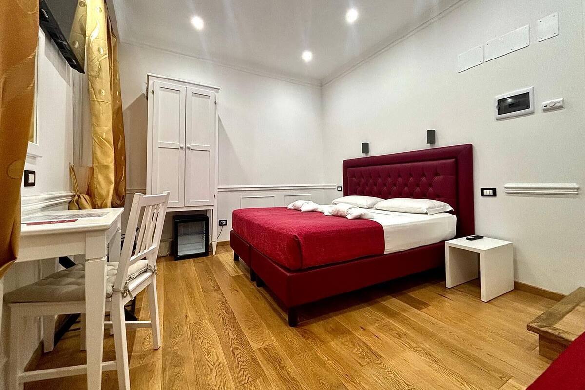 A bedroom with a red bed, white walls, and a wooden floor.