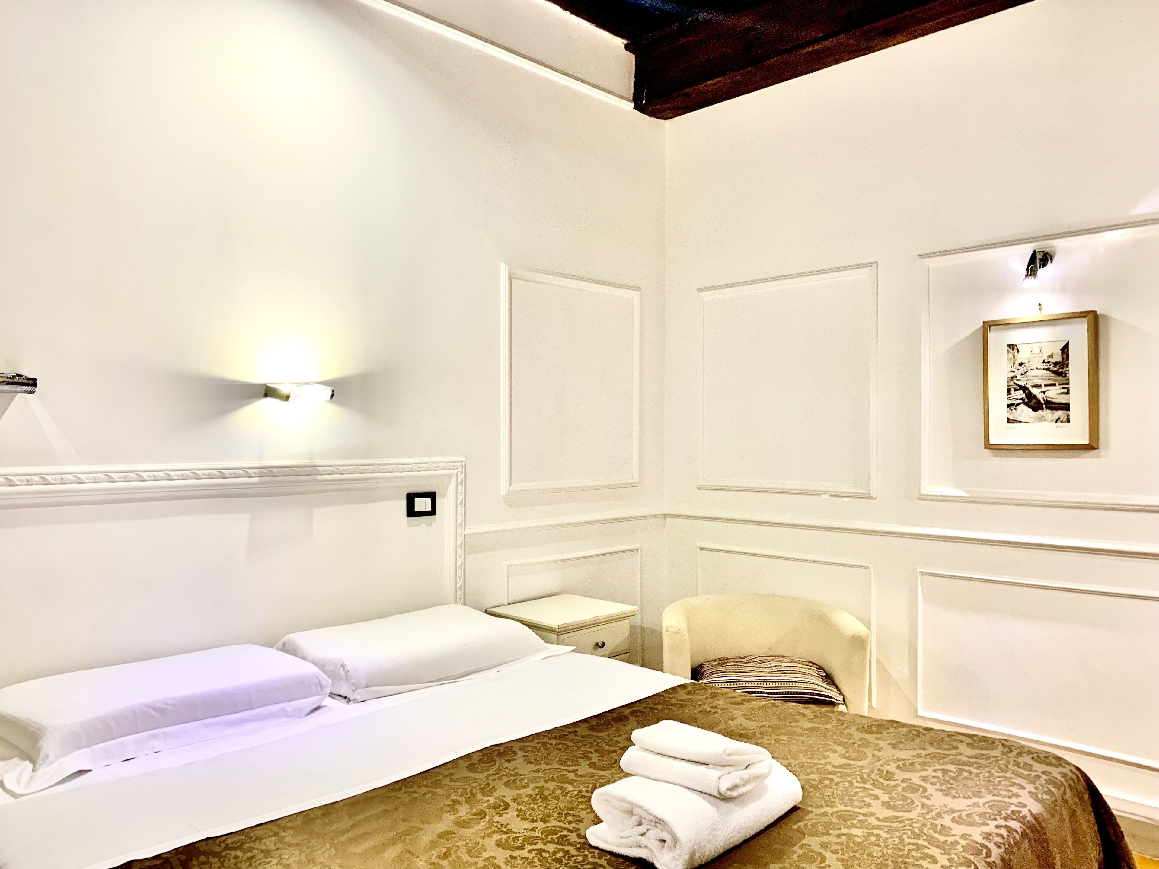 Camera d'albergo con un letto, una sedia, un comodino e una lampada a parete.