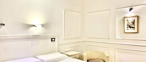 Camera d'albergo con un letto, una sedia, un comodino e una lampada a parete.