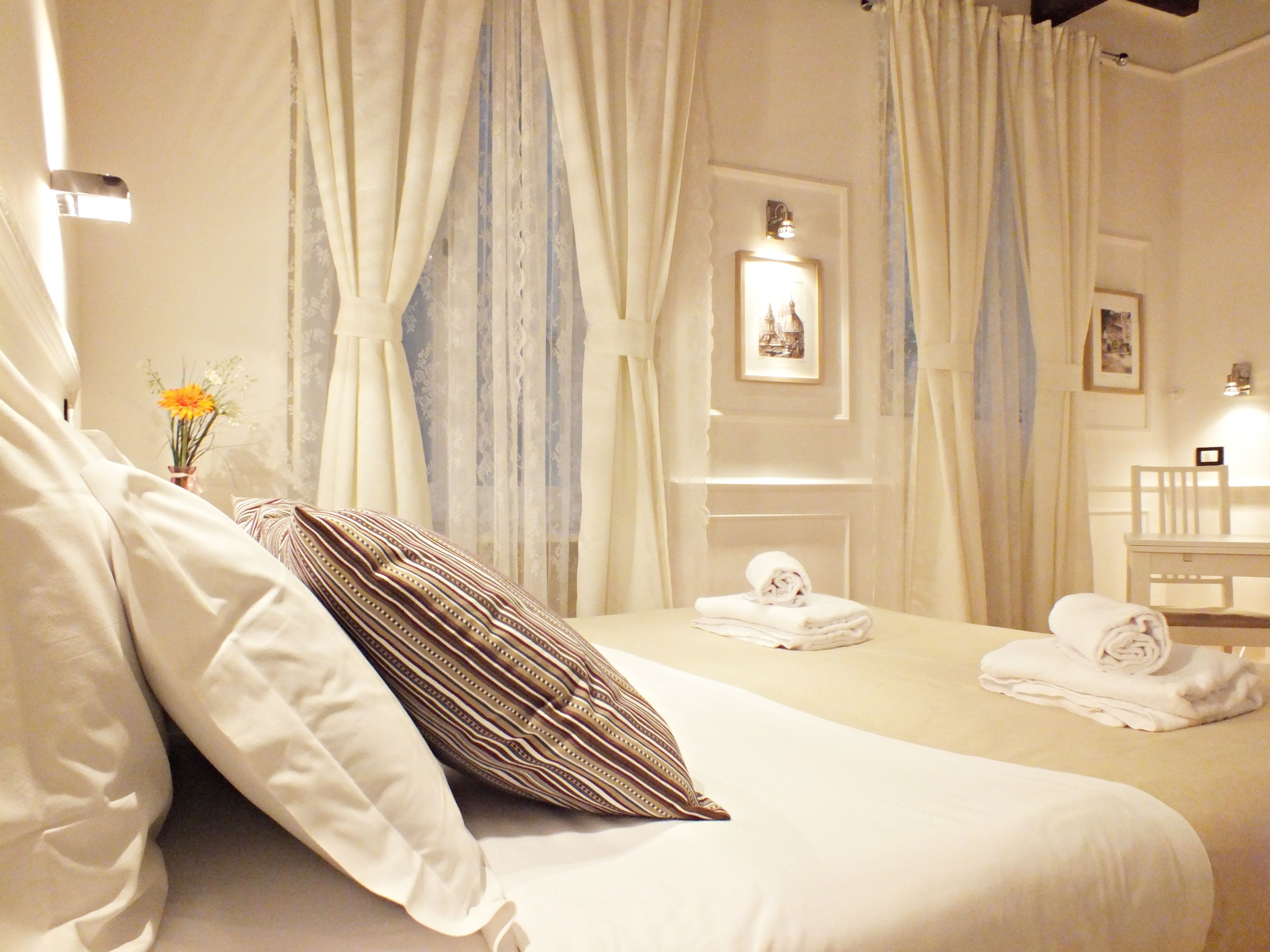 A hotel room with a bed, a chair, a table, and a vase with flowers.