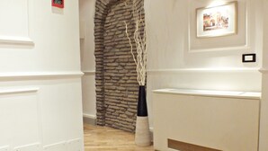 A hallway with wooden flooring, white walls, and a stone archway. There is a framed picture on the wall and a white reception desk. - Domus Ester Roma (Rome)