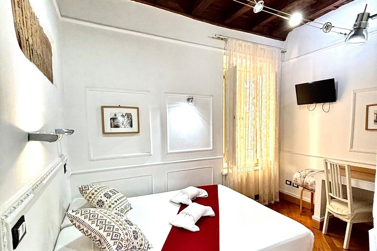 A hotel room with a bed, a desk, a chair, a TV, and a remote control on the nightstand.