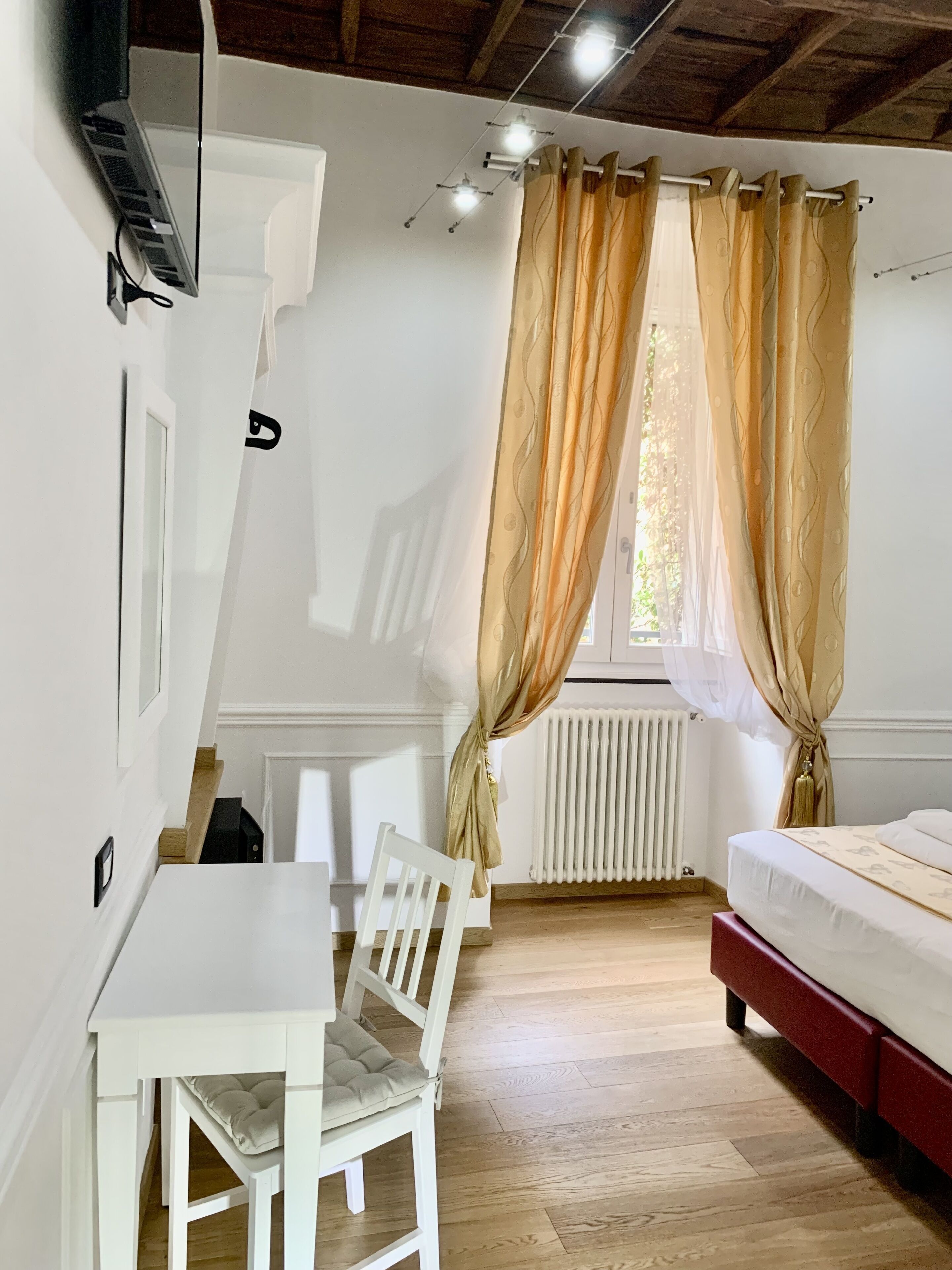 A room with a white table, a white chair, a bed with a red headboard, and a window with curtains.