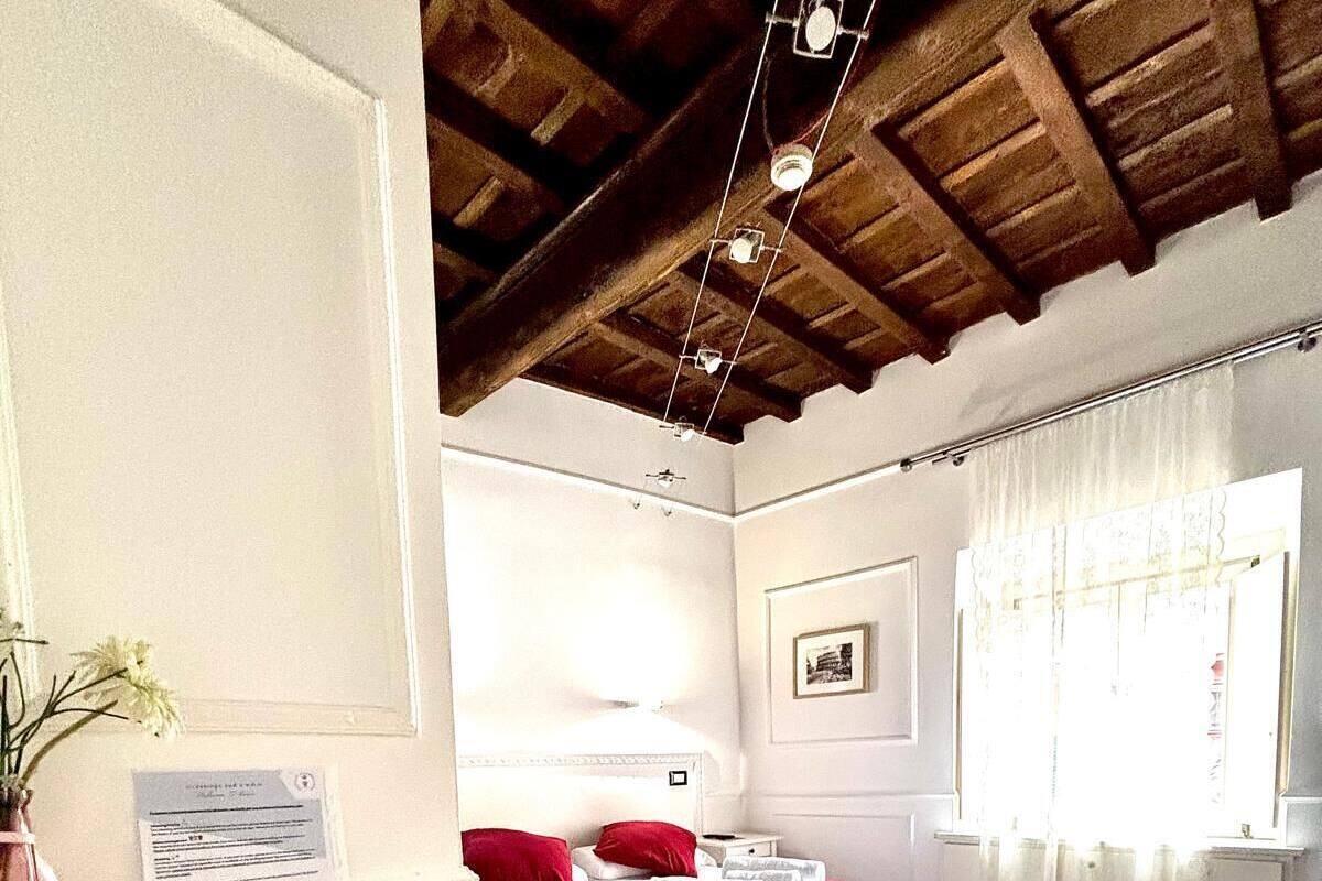 A bedroom with a wooden floor, a bed with red and white bedding, a bedside table, and a window with curtains.