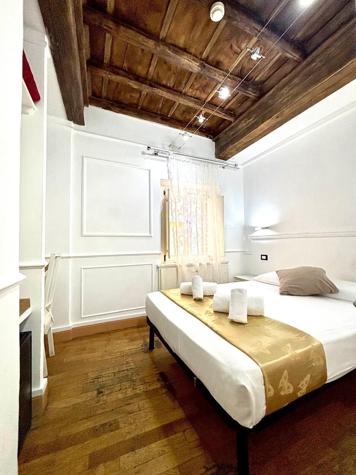 A bedroom with a wooden ceiling, a bed with white linens, a bedside table, and a window with a curtain.