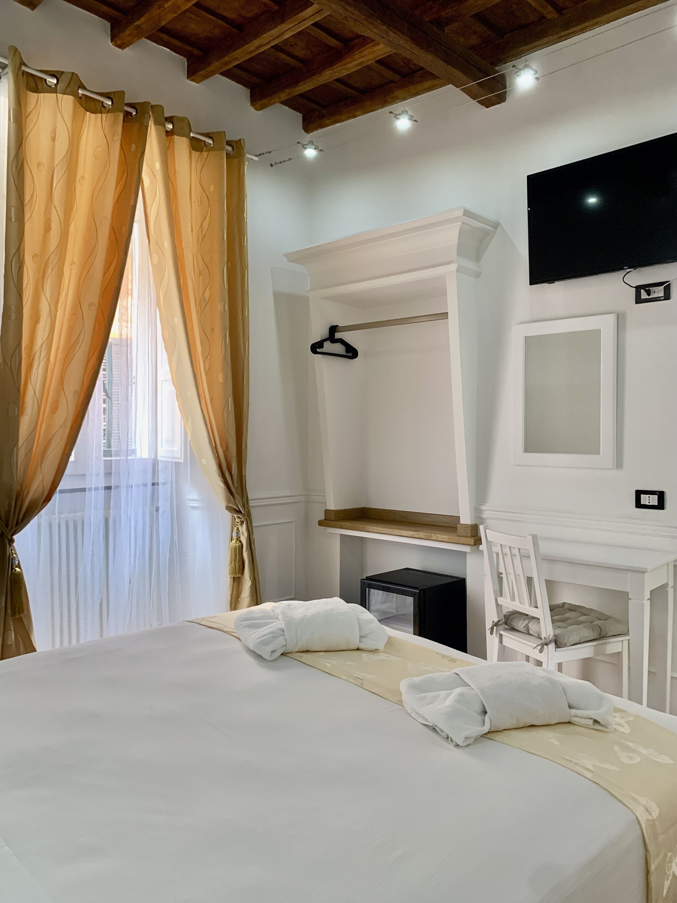 Un dormitorio con cama, escritorio, silla, televisión y ventana con cortinas.