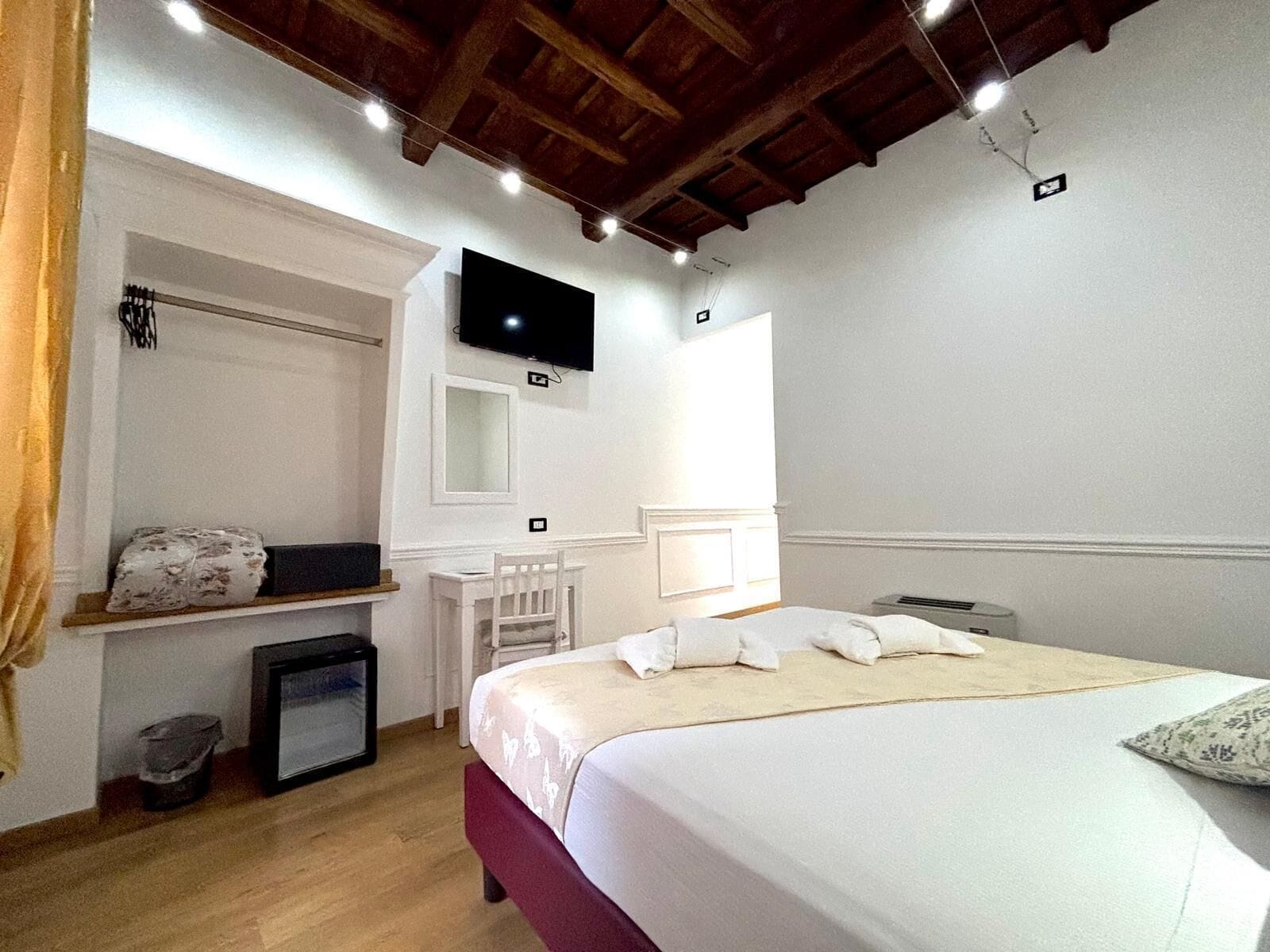 A hotel room with a bed, a TV mounted on the wall, a small desk, and a mirror.