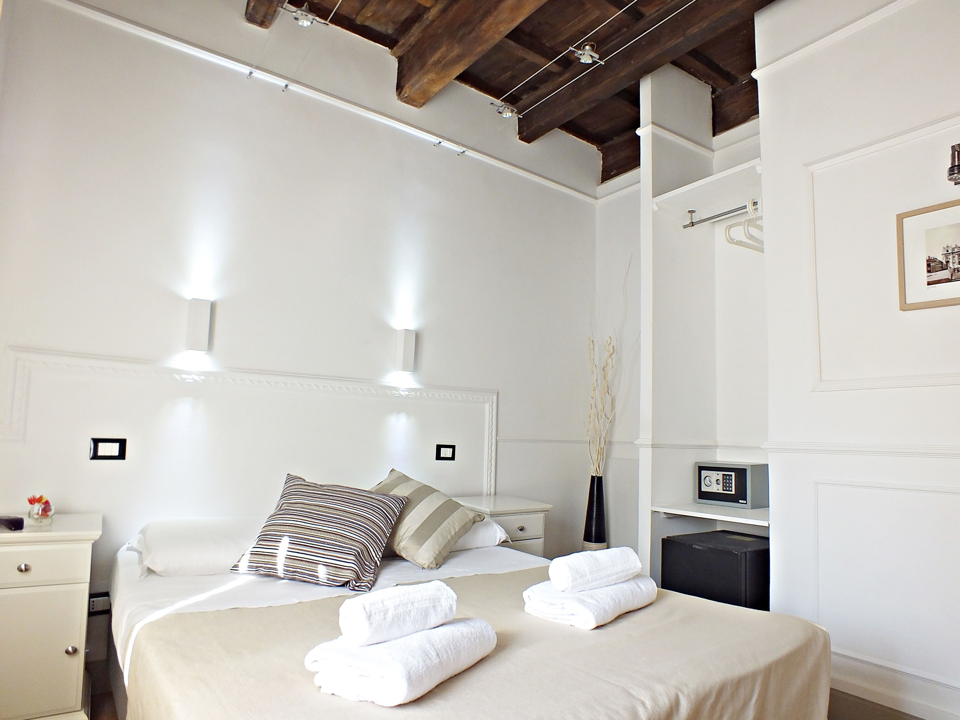 A hotel room with a bed, bedside tables, a nightstand, a wall-mounted TV, and a framed picture.