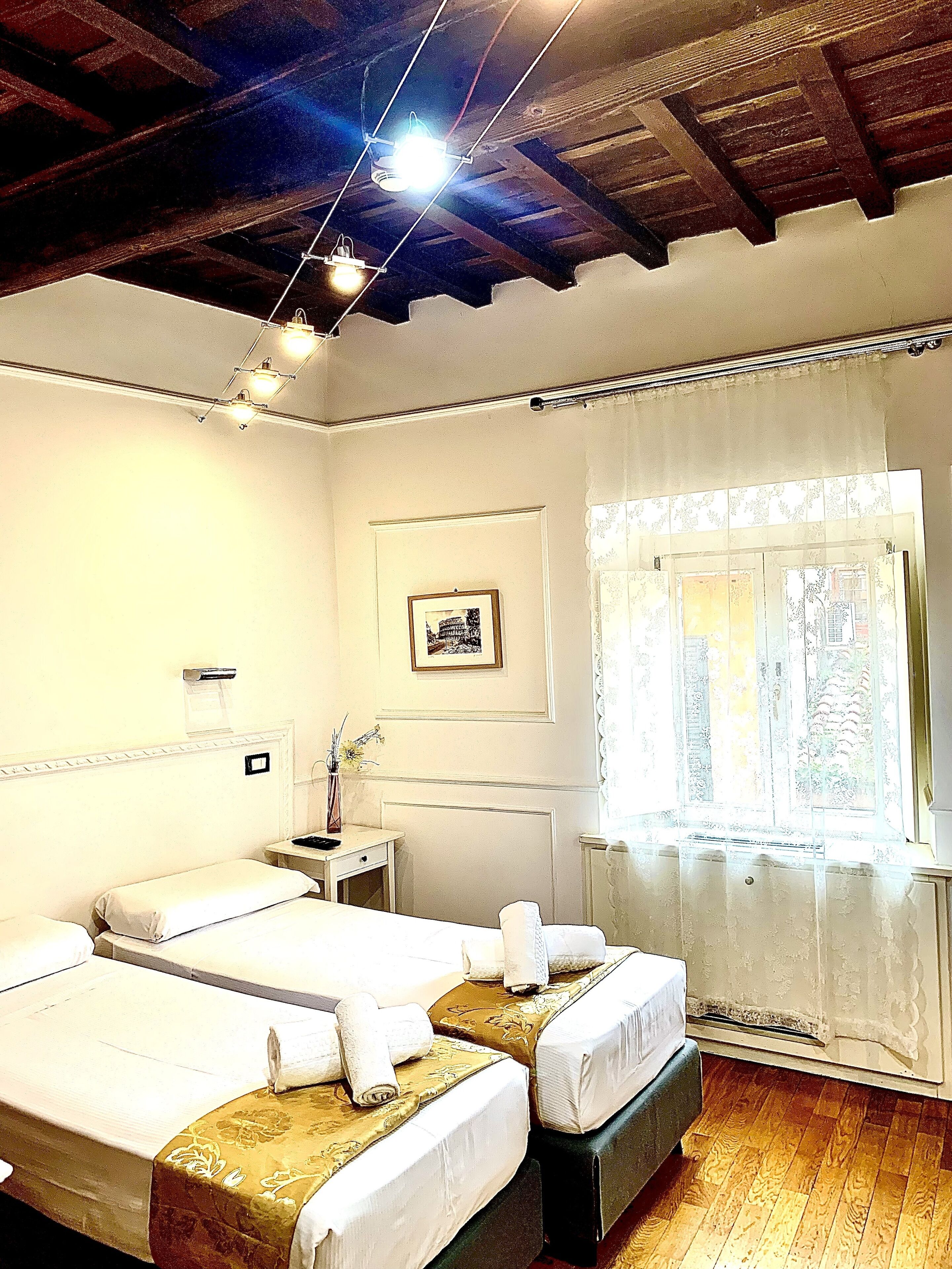 Habitación de hotel con dos camas, una mesita, una mesita de noche, un cuadro en la pared y una ventana con cortinas.