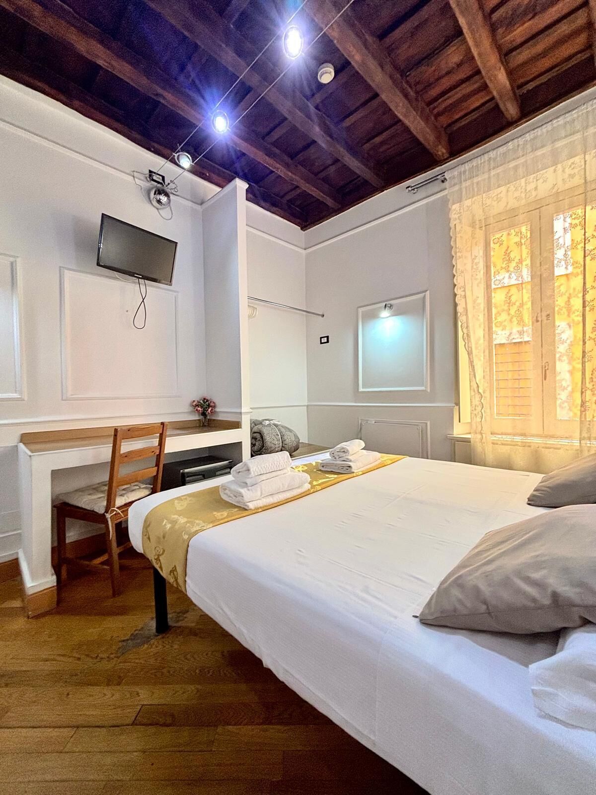 A bedroom with a bed, a desk, a chair, a television, and a window with curtains.