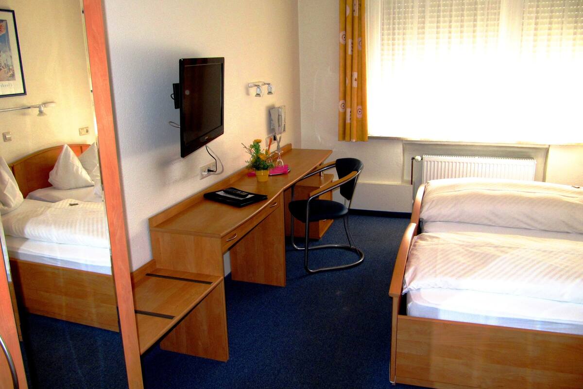 Habitación de hotel con cama, escritorio, silla, televisor y ventana con cortinas.