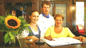 A reception desk with a large sunflower, a wooden counter, and a person holding a book. - Hotel-Gasthof am Selteltor (Wiesensteig)