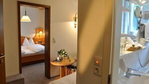 A hotel room with a bed, a small table with a vase, a mirror, and a bathroom with a sink and toilet. - Hotel-Gasthof am Selteltor (Wiesensteig)