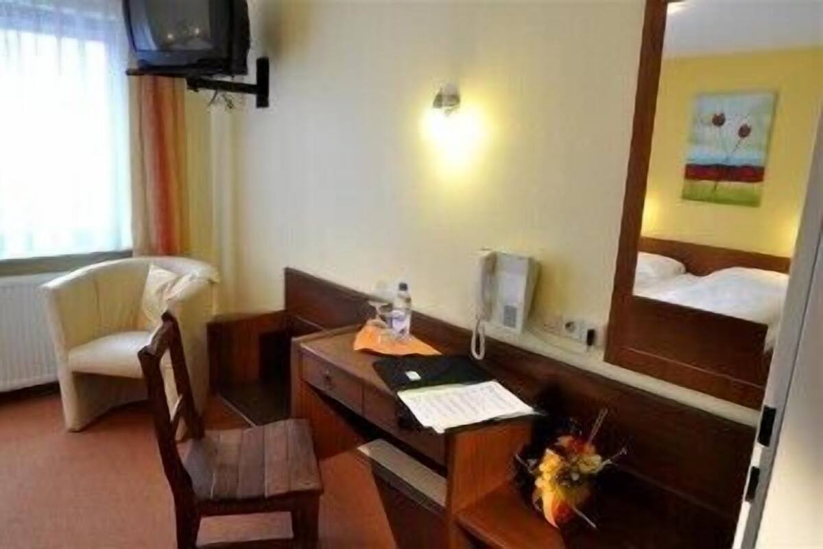 Habitación de hotel con cama, escritorio, silla, teléfono y televisor montado en la pared.