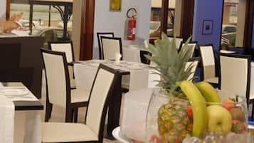 A dining area with tables set for service, chairs, and a decorative centerpiece with fruits and bottles.