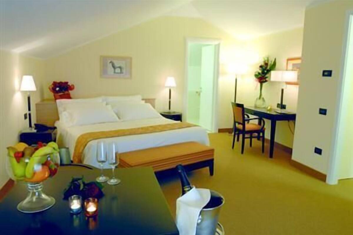 Habitación de hotel con cama, mesitas de noche, un escritorio y una silla. Hay lámparas, un frutero y una botella en el escritorio.