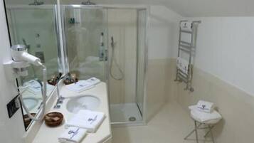 A modern bathroom with a glass-enclosed shower, a sink with a mirror, and a small stool.