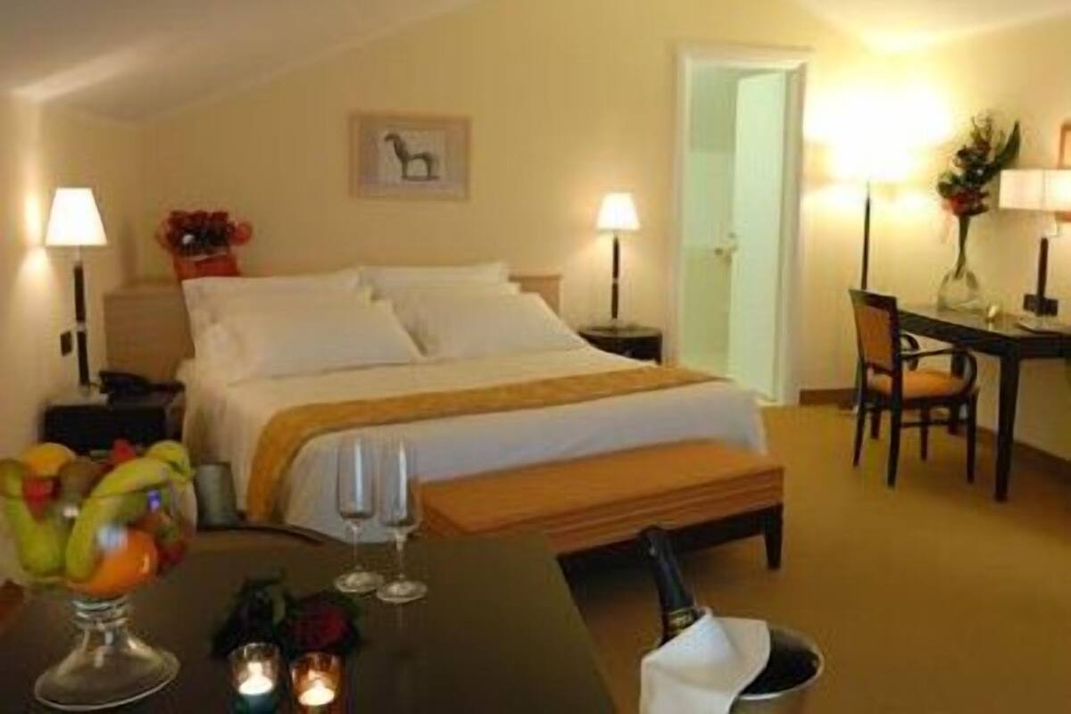 Una habitación de hotel con cama, lámparas de noche, una mesita con frutero, copas de vino y una botella de champán.