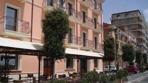 Una hilera de edificios de varios pisos con balcones, mesas al aire libre y plantas en macetas.