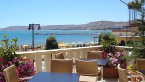 Una terraza con sillones y mesas de mimbre, con vistas a la costa y un cielo despejado.