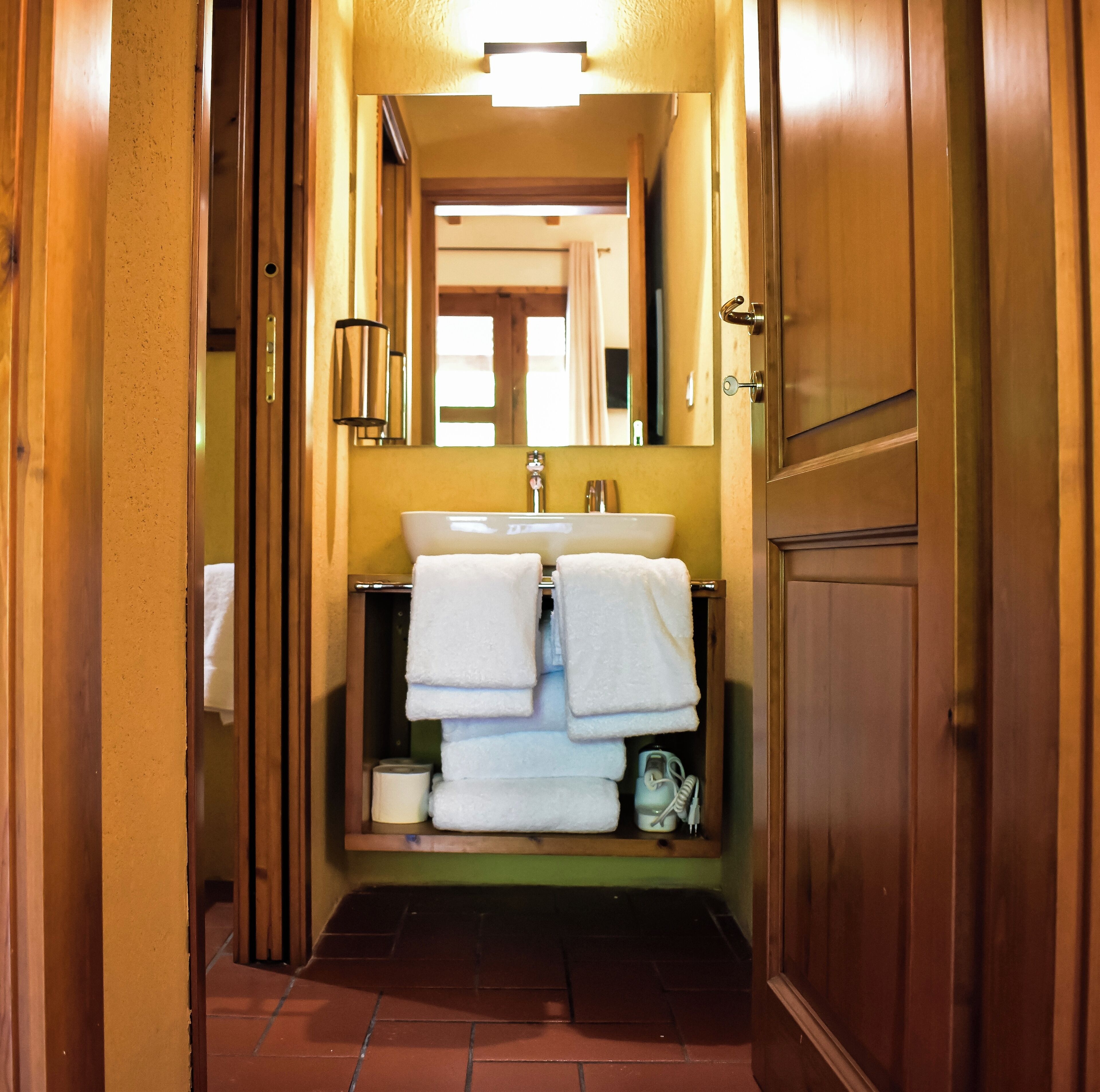 Un couloir étroit mène à une salle de bain équipée d’un lavabo, de deux serviettes, d’un miroir et d’un porte-serviettes.