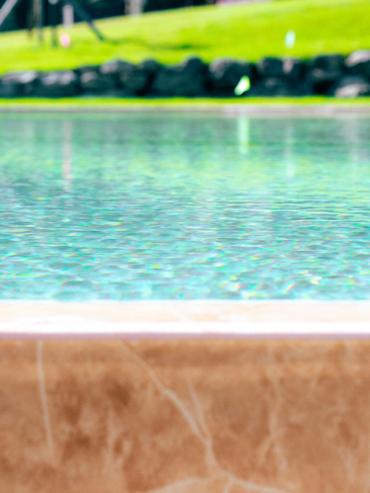 Une piscine dont le bord est recouvert de carrelage, avec une zone herbeuse en arrière-plan.